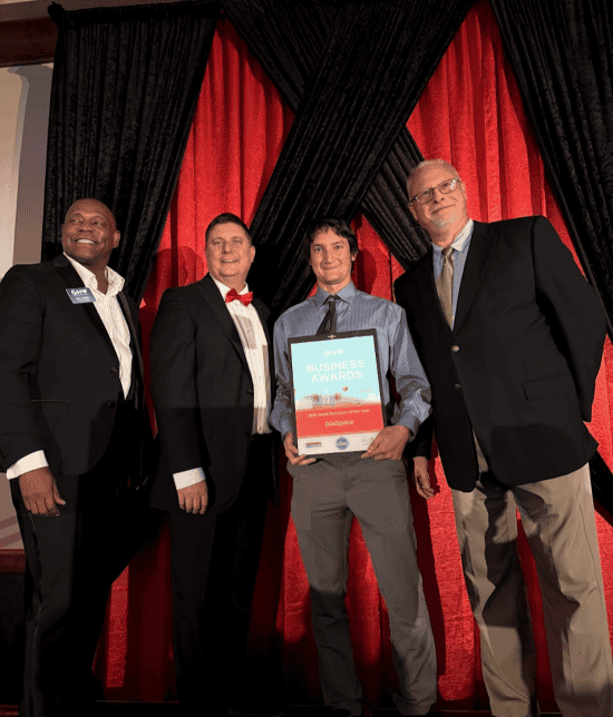 - GiaSpace: IT Support & Cybersecurity for Florida Businesses Four men in formal attire on a stage, with one holding a framed award certificate against red curtains in the background.