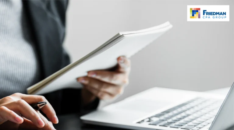 Professional person typing on a laptop while holding a folder, with the Friedman CPA Group logo in the top-right corner