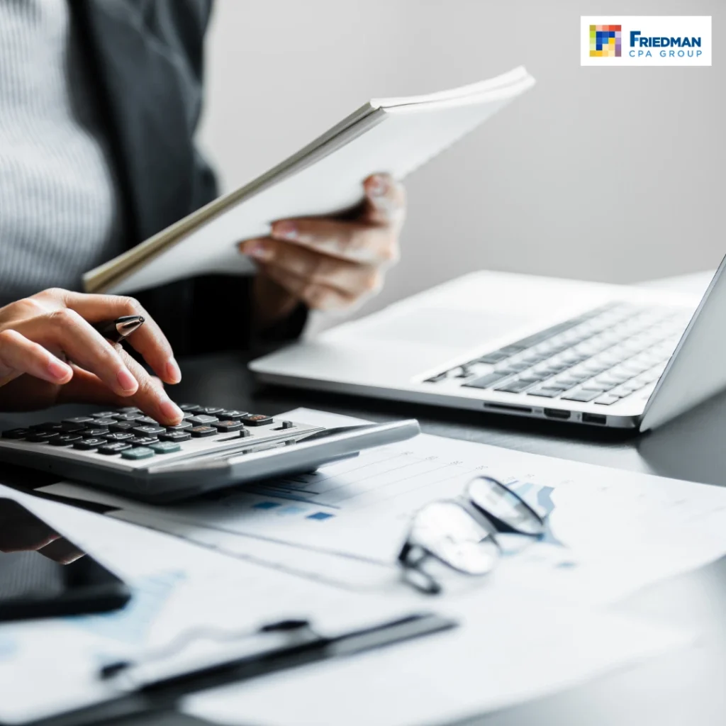 - GiaSpace: IT Support & Cybersecurity for Florida Businesses Businessperson calculating numbers with a calculator beside a laptop and financial documents; Friedman CPA Group logo visible.