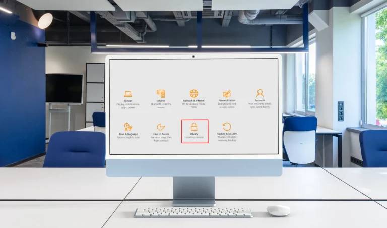 Large computer monitor on a white desk displaying Windows settings with Privacy tile highlighted in orange.