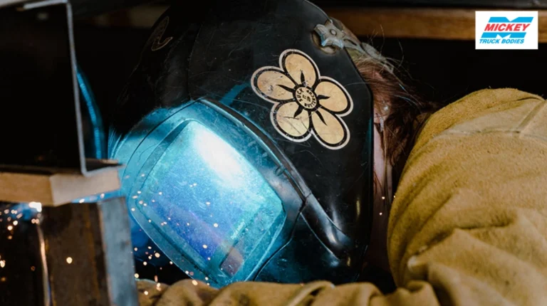 Welding worker in a dark protective helmet with a glowing blue visor, sparks flying as metal is welded.